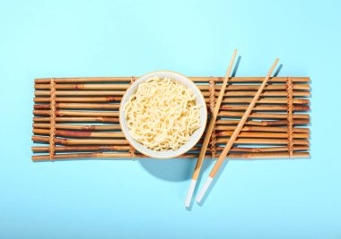 Lezzetli erişteli kase ve mavi arka planda çubuklar.