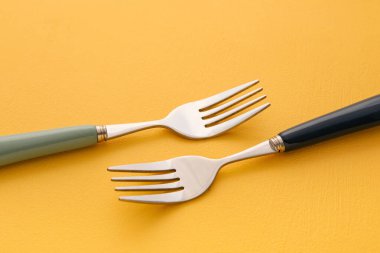 Sarı zemin üzerinde paslanmaz çelik çatallar, yakın plan.