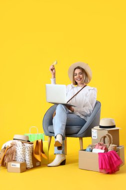 Sarı arka planda dizüstü bilgisayarı ve kredi kartı olan genç bir kadın. İnternetten alışveriş
