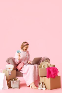 Pembe arka planda kredi kartı ve laptopu olan genç bir kadın. İnternetten alışveriş