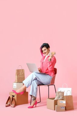 Kredi kartı ve dizüstü bilgisayarı olan güzel bir kadın pembe arka planda online alışveriş yapıyor.