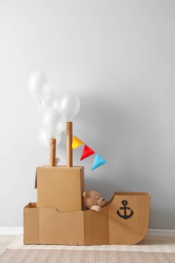 Işık duvarının yanında balonları olan oyuncak karton gemi.
