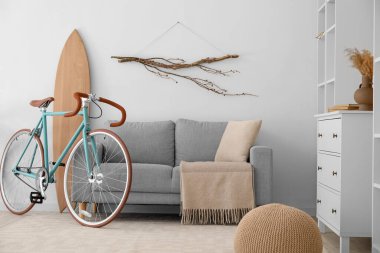 İçinde bisiklet, gri kanepe ve sörf tahtası olan modern oturma odası.