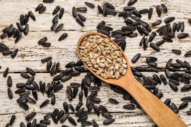 Beyaz ahşap arka planda ayçiçeği tohumlu kaşık, yakın plan.