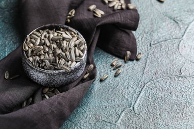 Koyu arkaplanda bir kase ayçiçeği çekirdeği ve peçete.