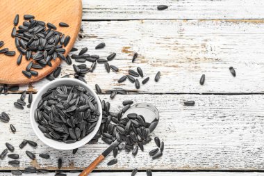 Beyaz ahşap arka planda siyah ayçiçeği tohumlu kase ve kaşık.