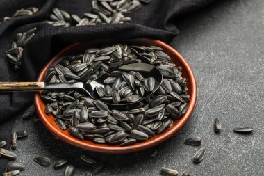 Koyu arkaplanda siyah ayçiçeği tohumları olan kase, kaşık ve peçete.