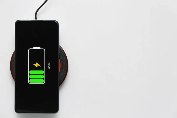 Modern mobile phone charging with wireless pad on grey background