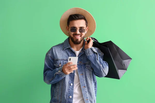 Schöner Mann Mit Handy Und Einkaufstaschen Auf Grünem Hintergrund — Stockfoto