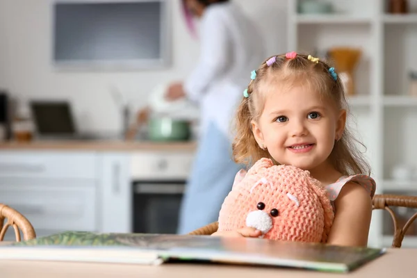 Liten Flicka Med Leksak Och Bok Sitter Vid Bordet Och — Stockfoto