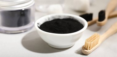 Aktif kömür diş tozu ve arka planda fırça ile kase, yakın plan.