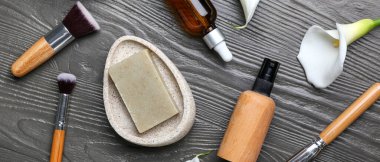 Koyu ahşap arka planda kozmetik ürünler ve makyaj fırçaları.