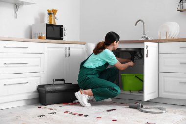 Kadın tesisatçı mutfakta lavabo tamir ediyor.
