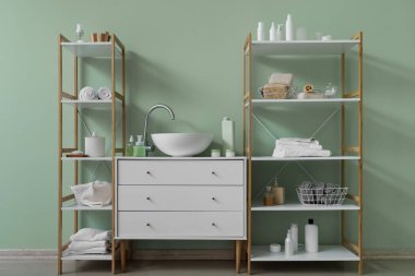 Küvetli çekmeceler, raf üniteleri ve yeşil duvarın yanındaki banyo aksesuarları.