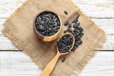 Beyaz ahşap arka planda bir kase dolusu siyah ayçiçeği çekirdeği.