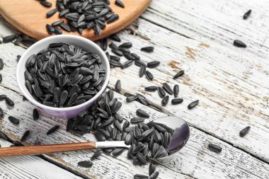 Beyaz ahşap arka planda siyah ayçiçeği tohumlu kase ve kaşık.