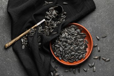 Koyu arkaplanda siyah ayçiçeği tohumları olan kase, kaşık ve peçete.