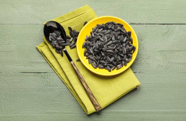 Siyah ayçiçeği tohumları, yeşil ahşap arka planda kaşık ve peçete.