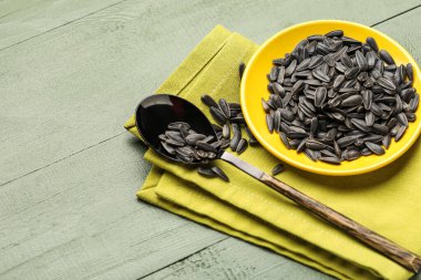 Siyah ayçiçeği tohumları, yeşil ahşap arka planda kaşık ve peçete.