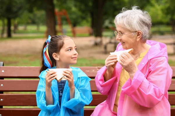 Κοριτσάκι Και Γιαγιά Της Τρώνε Σάντουιτς Στο Παγκάκι Στο Πάρκο — Φωτογραφία Αρχείου