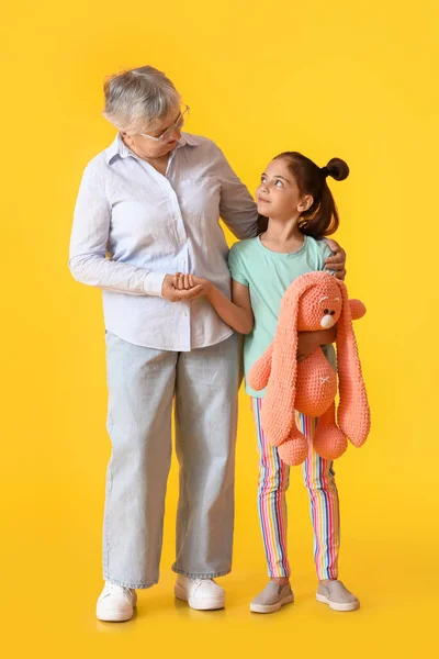 Κοριτσάκι Παιχνίδι Και Γιαγιά Της Αγκαλιάζονται Κίτρινο Φόντο — Φωτογραφία Αρχείου