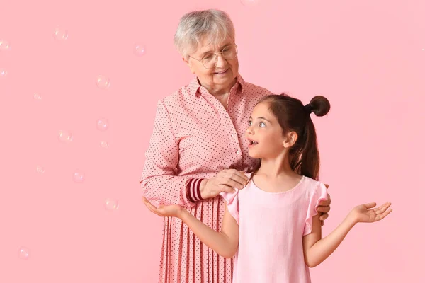 Старша Жінка Своєю Маленькою Онучкою Мильними Бульбашками Рожевому Фоні — стокове фото