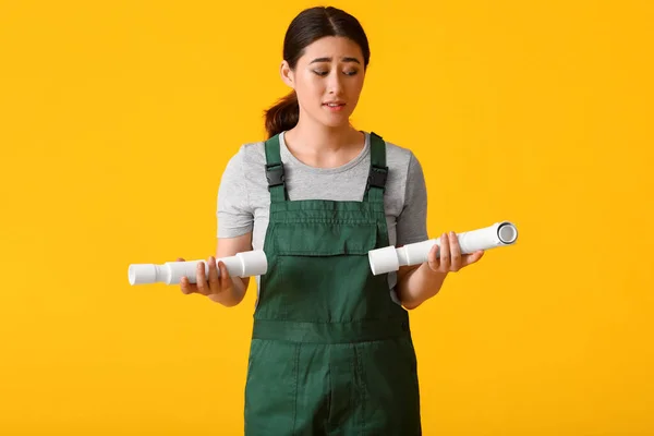 Asian female plumber with flexible hoses on yellow background