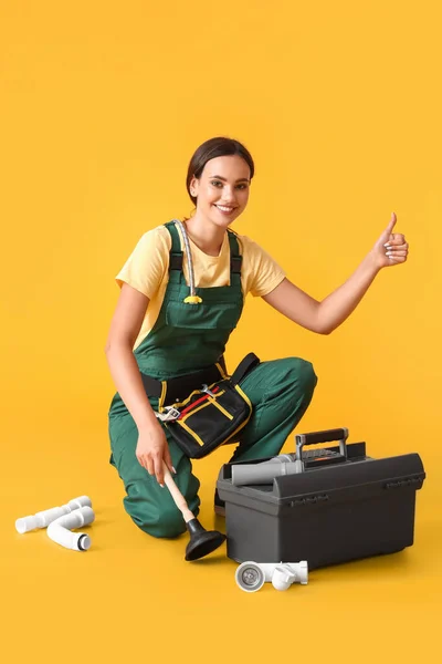 Female plumber with tools showing thumb-up on yellow background