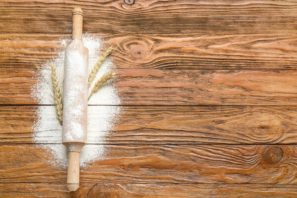 Пшеничные уши со скалкой и мукой на деревянном фоне