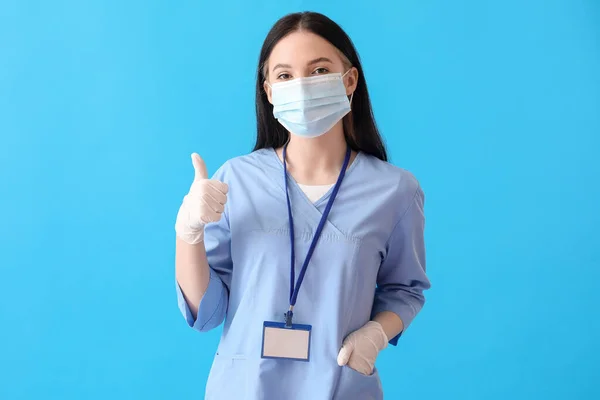青の背景に親指アップを示すマスクの女性医療アシスタント — ストック写真