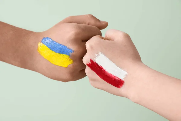 Volunteers with drawn flags of Ukraine and Poland bumping fists on green background