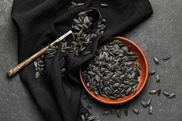 Koyu arkaplanda siyah ayçiçeği tohumları olan kase, kaşık ve peçete.