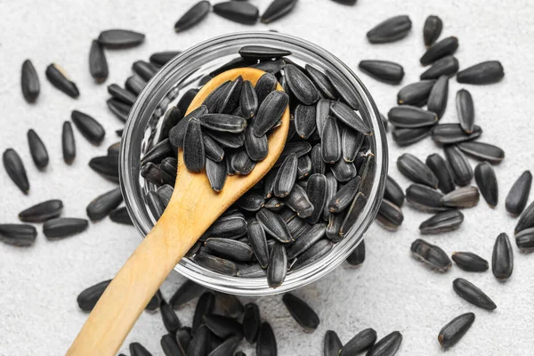 Beyaz arka planda kaşık ve siyah ayçiçeği tohumları olan bir kâse.