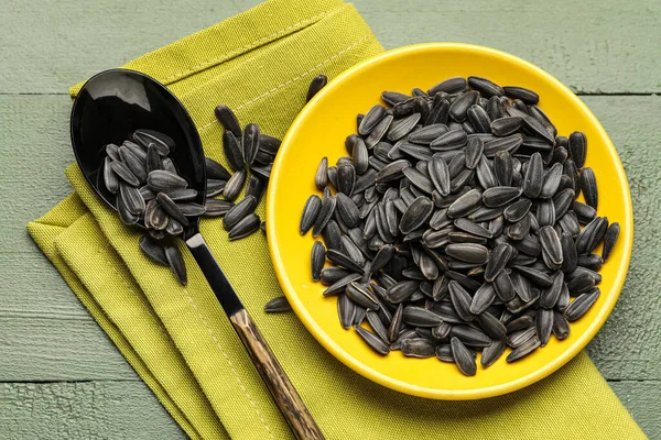 Siyah ayçiçeği tohumları, yeşil ahşap arka planda kaşık ve peçete.