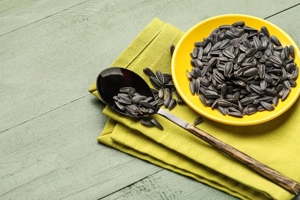 Siyah ayçiçeği tohumları, yeşil ahşap arka planda kaşık ve peçete.