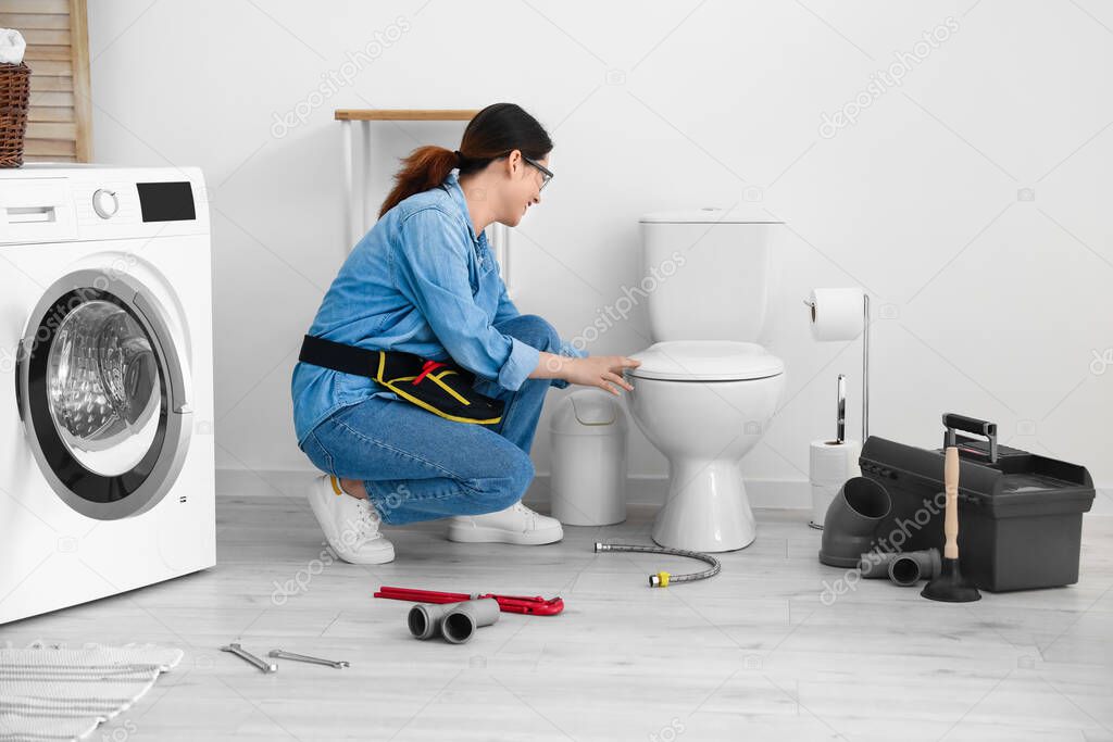 Asian female plumber fixing toilet bowl in bathroom