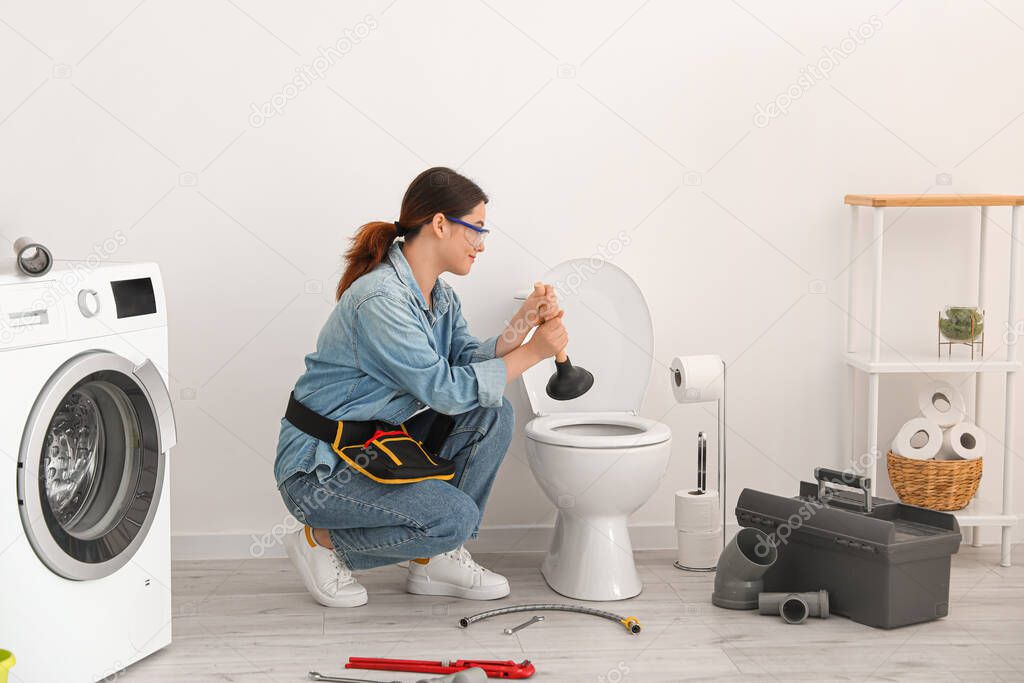 Asian female plumber with plunger fixing toilet bowl in bathroom