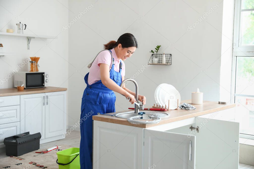 Asian female plumber fixing sink with plunger in kitchen