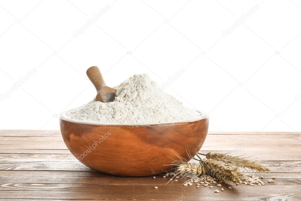 Bowl with flour, scoop and wheat ears on wooden table against white background