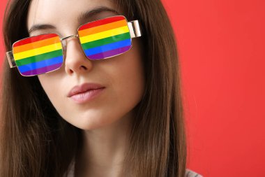 Kırmızı arka planda şık gökkuşağı güneş gözlüklü güzel genç bir kadın. LGBT kavramı