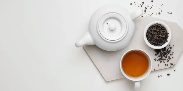 Teapot, cup of tea and dry leaves in bowl on white background with space for text