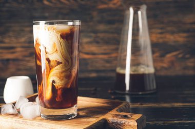 Koyu ahşap masada bir bardak soğuk kahve ve buz.