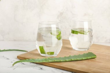 Aloe suyu bardakları ve açık arkaplanda yaprakları olan tahta