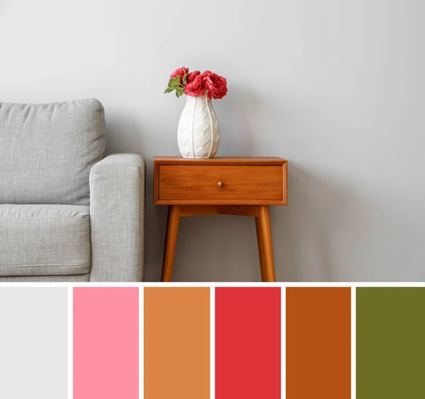 Vase with flowers on table and grey sofa near light wall. Different color patterns