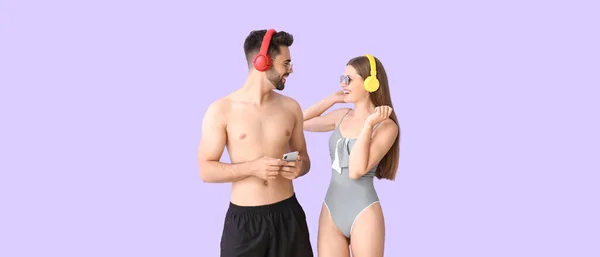 Glückliches Junges Paar Badebekleidung Hört Musik Auf Fliederfarbenem Hintergrund — Stockfoto