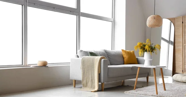 Sofa and table with bouquet of mimosa flowers in interior of living room