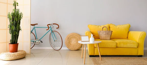 Interior of light living room with yellow sofa, folding screen and bicycle