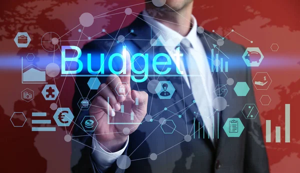 Businessman touching word BUDGET on virtual screen against red background, closeup