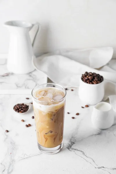 Glass of cold brew with milk and coffee beans on white marble table