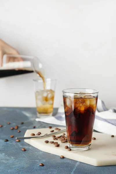 Glass of cold brew and coffee beans on color table against white background